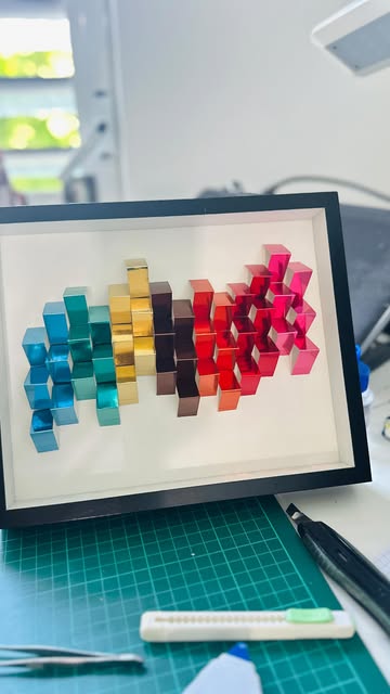 Chromatic Rise: metallic paper cubes from teal to gold to pink in a black shadow box
